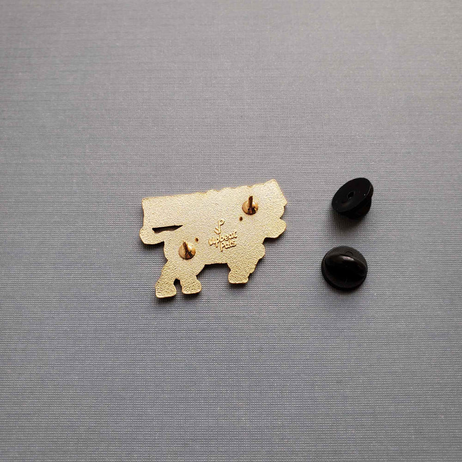 The back of a gold plated enamel pin of a bull goring the I and M in the word impossible, transforming it into possible. The word possible appears in black letters above the bull, who is charging slightly upward. This pin sits on textured gray background.