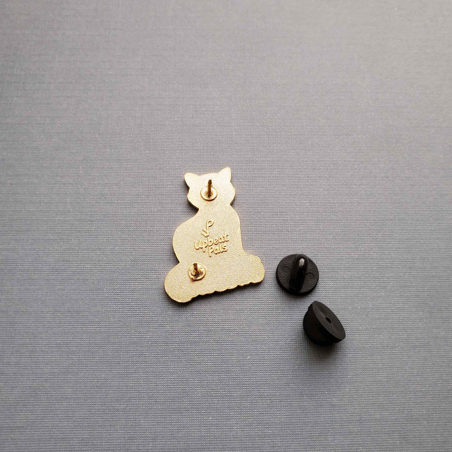 The back of a gold plated enamel pin of a cat perched on top of the word lucky, in black letters. The cat's forepaws rest on the letters U and N, to transform the word from unlucky into lucky. This lapel pin sits on a gray textured background.