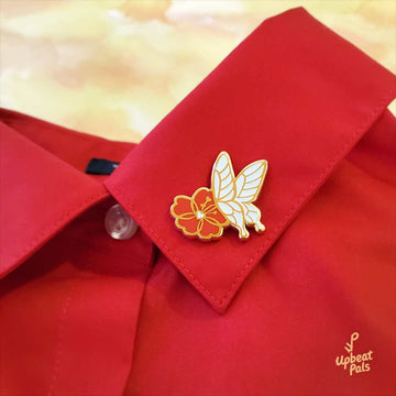 A gold plated enamel pin featuring a white butterfly landing on a red flower. This lapel pin is shown affixed on the neck collar of a red dress shirt.