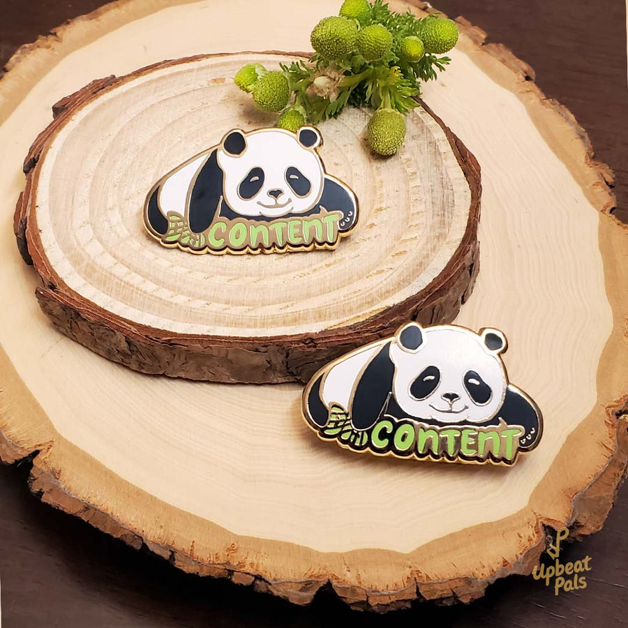 Two gold plated enamel pins of a panda laying down, on top of the word content in green letters. The panda's right arm is covering the prefixed 